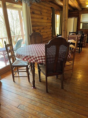 A wooden interior with a dining table set for four, surrounded by chairs with woven backs.