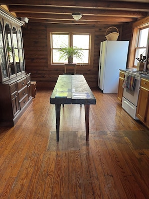 Une cuisine rustique avec un plancher en bois, une table en bois, un réfrigérateur et une cuisinière.