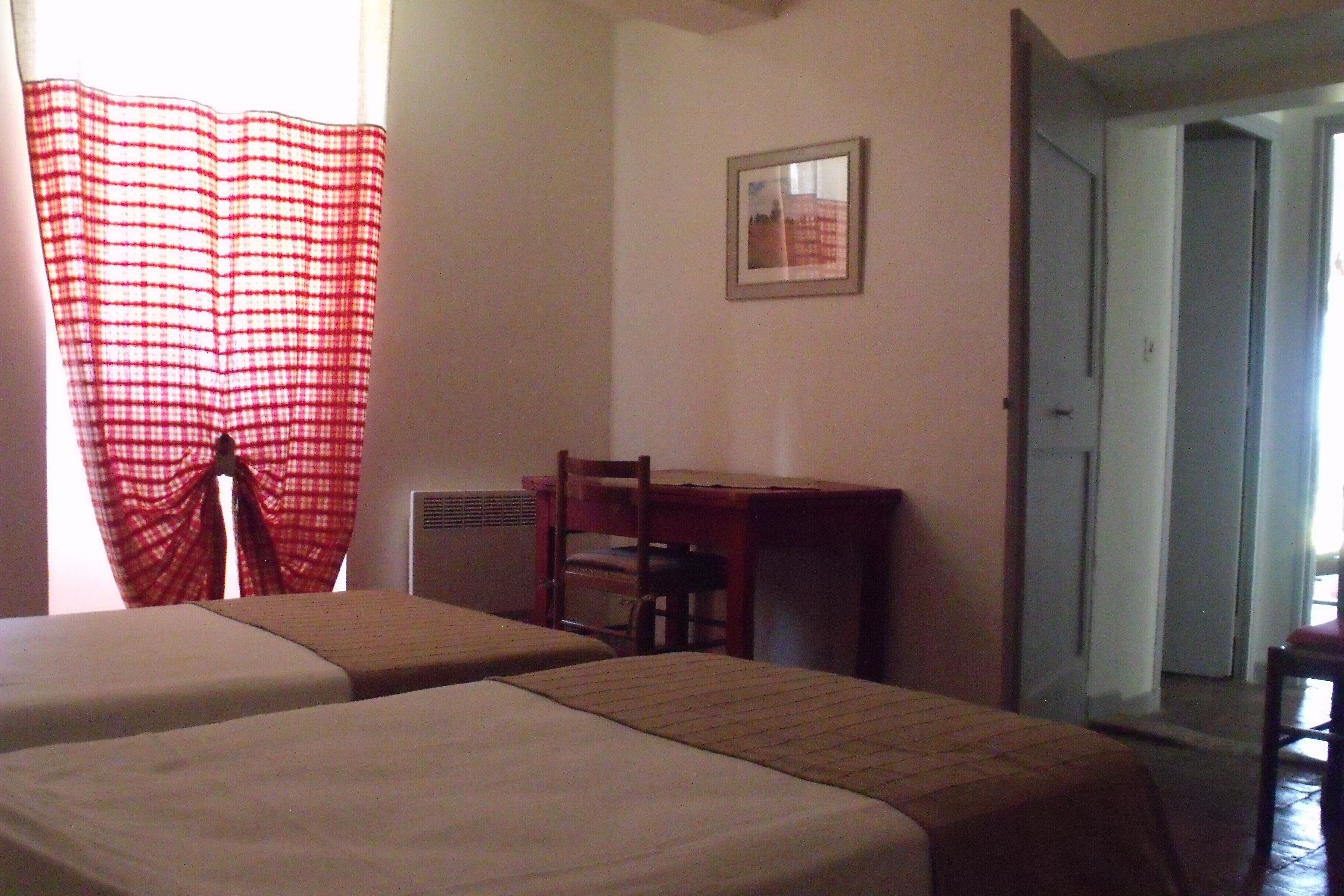 A room with two beds, a desk, a chair, and a framed picture on the wall.