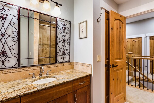 A bathroom with a marble sink, wooden cabinets, and a large mirror with decorative metalwork.