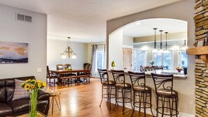 A spacious dining area with a wooden table and chairs, a bar with stools, and a kitchen area with a stone accent wall. - Large Comfortable home with Flatiron views (Boulder)