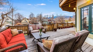 A wooden deck with outdoor furniture, a view of a mountain range, and a building with a balcony. - Large Comfortable home with Flatiron views (Boulder)