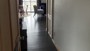 Un pasillo con piso de madera oscura, un tapete estampado y vistas a un balcón con una silla y una mesa.