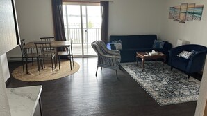 Una sala de estar con piso de madera oscura, una mesa de comedor con sillas, un sillón a rayas, un sofá azul y un tapete estampado.