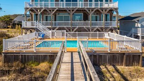 A two-story beachfront house with a wooden deck, a swimming pool, and multiple balconies. - Big Kahuna | Ocean Front, Pool, Elevator, Decks + Beach Access (Kure Beach)