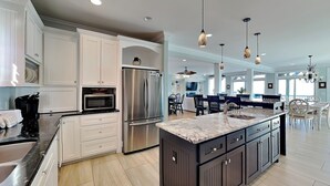 A spacious kitchen with white cabinetry, a stainless steel refrigerator, and a large island with a marble countertop. - Big Kahuna | Ocean Front, Pool, Elevator, Decks + Beach Access (Kure Beach)
