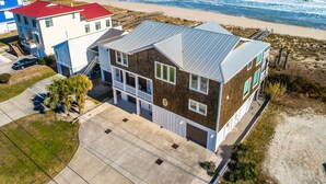 A beachfront property with a two-story house, a red-roofed building, and a beach view. - Big Kahuna | Ocean Front, Pool, Elevator, Decks + Beach Access (Kure Beach)