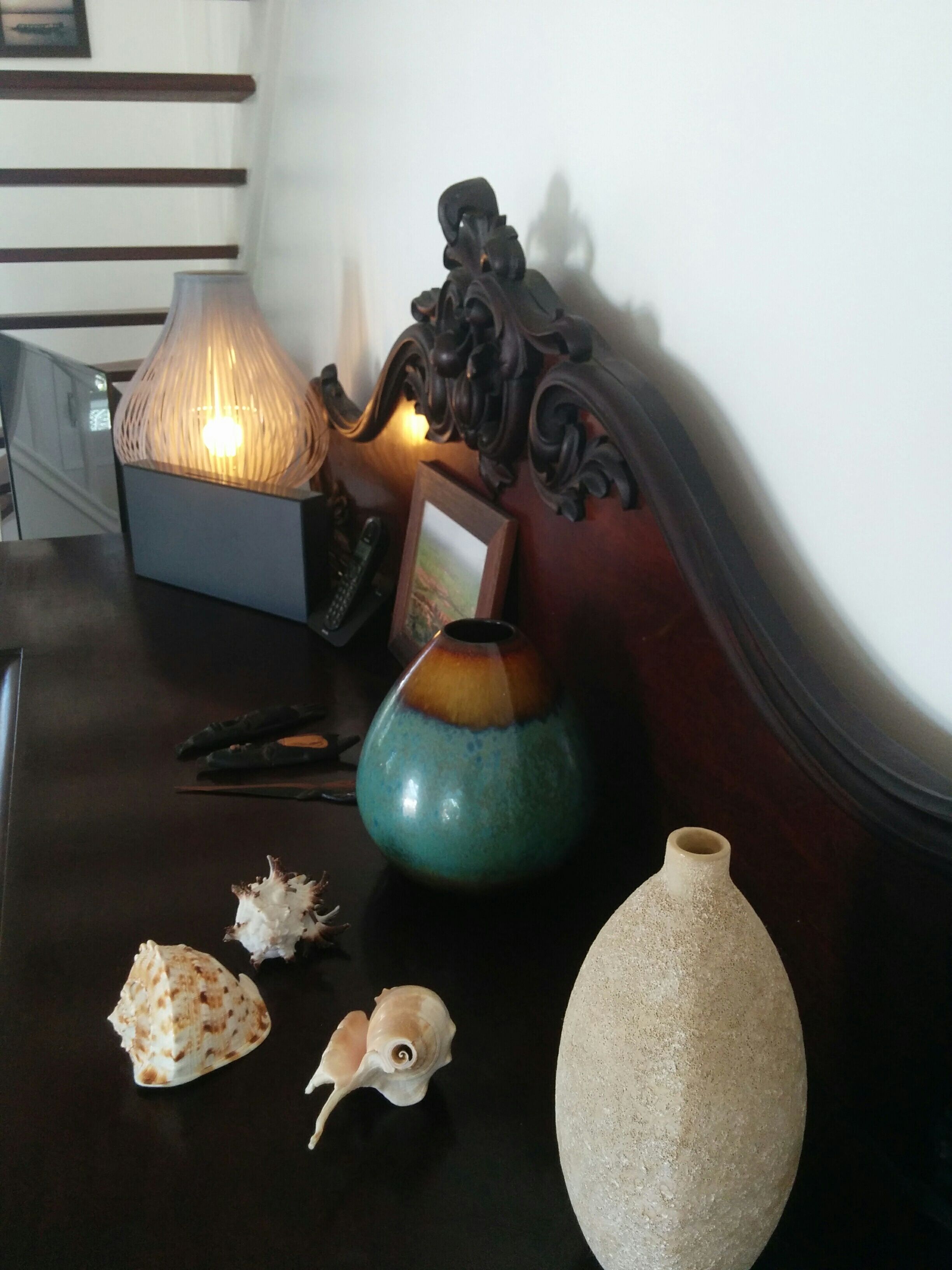 Une table en bois, une lampe, un vase, des coquillages et un cadre photo.