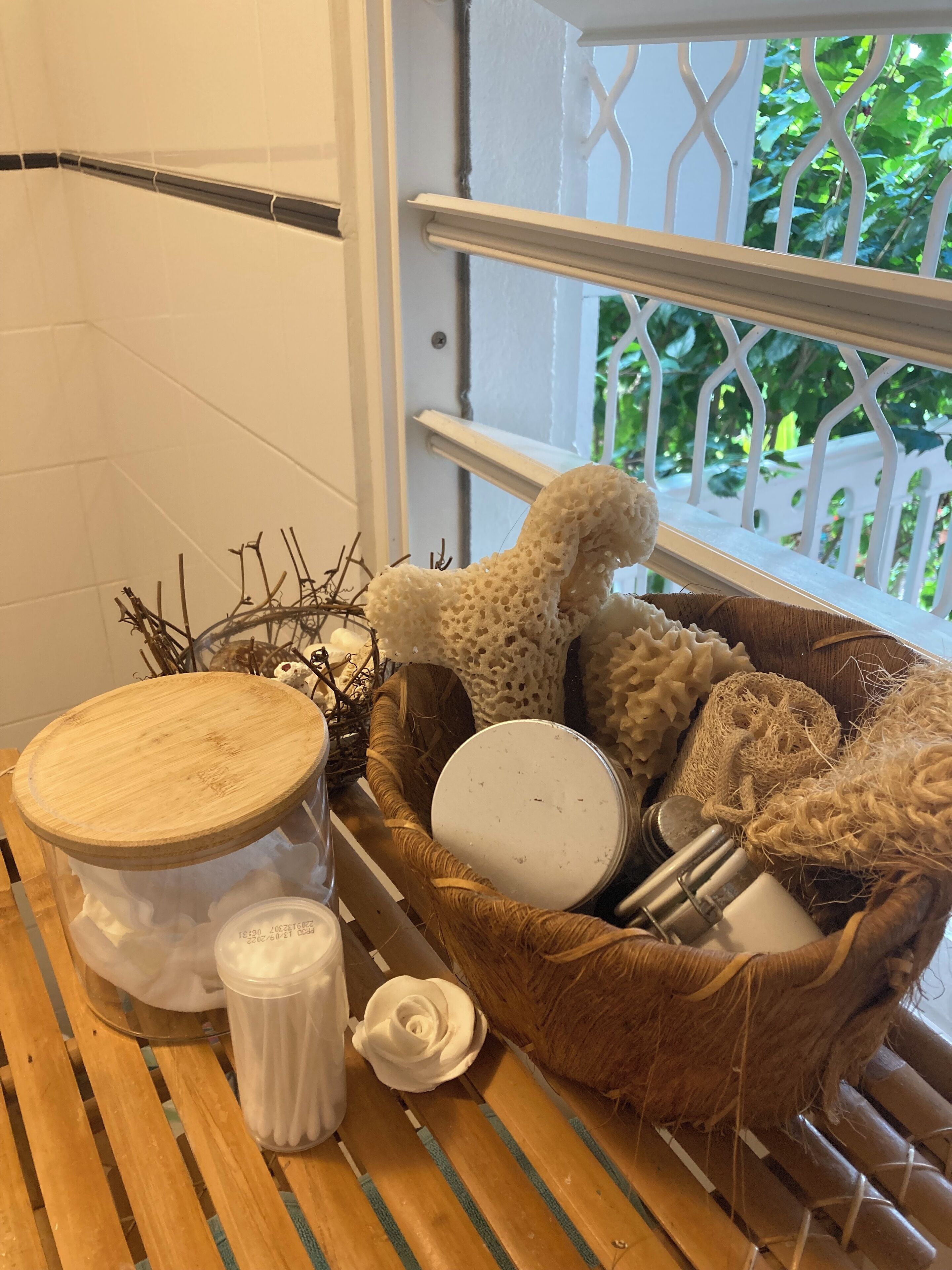 A bathroom with a wooden vanity, a wicker basket with toiletries, and a view of greenery outside.