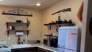 Een keuken met een witte koelkast, kookplaat en magnetron. Er zijn houten kastjes en een rundleer aanrecht.