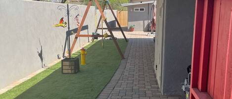 A backyard with a brick pathway, a swing set, and a red fence.