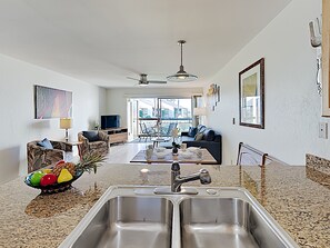 A modern kitchen with a double sink, a dining area with a table and chairs, a sofa, and a television.