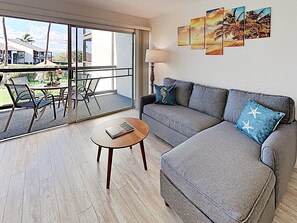 A modern living room with a grey sofa, a coffee table, and a view of a balcony with outdoor furniture.