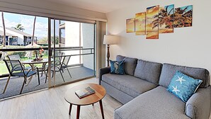 En moderne stue med en grå sofa, et sofabord og udsigt til en balkon med udendørs møbler.