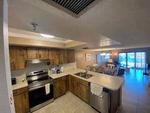 A modern kitchen with wooden cabinets, stainless steel appliances, and a central island with a sink. - Beautiful 1.5 BR Condo Steps Away from White Sandy Beaches (Madeira Beach)