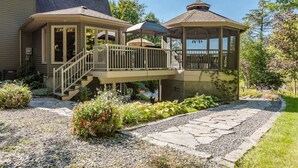 Ein Haus mit überdachter Veranda, einer Treppe zu einem oberen Stockwerk und einem Garten mit einem Kiesweg.