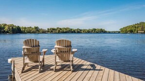 Ein Holzsteg mit zwei Adirondack-Stühlen, die auf einen stillen See blicken, umgeben von dichtem Grün.