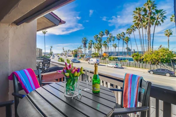 A balcony with a table, chairs, a bottle, and a vase of flowers.