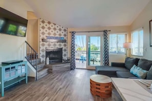 A living room with a fireplace, a sofa, a coffee table, and a staircase leading to a balcony.