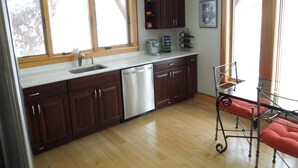 A kitchen with wooden cabinets, a dishwasher, a coffee maker, and a chair. - Modern Lakefront home (Hammondsport)