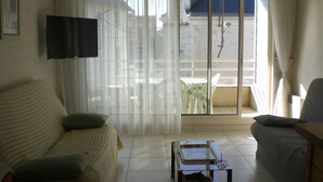 A living room with a sofa, a small table, and a TV mounted on the wall. - Well-located apartment, terrace with sea view. 50 m from the beach. For 2-4 pers    (Les Sables-D'olonne)