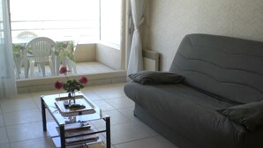 A living room with a grey sofa, a coffee table with a vase of flowers, and a view of the outside balcony. - Well-located apartment, terrace with sea view. 50 m from the beach. For 2-4 pers    (Les Sables-D'olonne)
