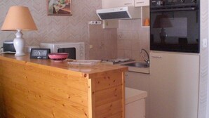 A compact kitchen with a microwave, toaster, sink, and oven. There's a wooden counter with a lamp and a bowl. - Well-located apartment, terrace with sea view. 50 m from the beach. For 2-4 pers    (Les Sables-D'olonne)