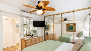 Ein Schlafzimmer mit einem Bett, einem Schminktisch, einem Fernseher, einem Deckenventilator und einem großen Spiegel.