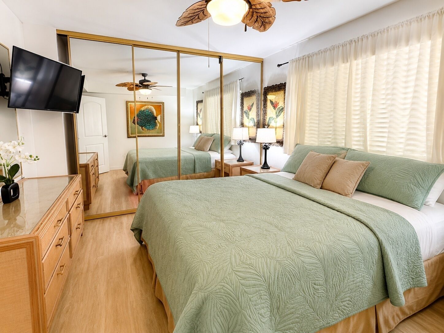 A bedroom with a bed, a TV, a mirror, and a ceiling fan.