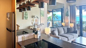 Eine moderne Küche mit Kühlschrank, ein Essbereich mit Tisch und Stühlen sowie ein Wohnzimmer mit Sofa und Meerblick.