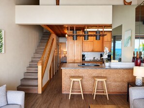 A modern kitchen with a wooden island, bar stools, and a view of the ocean.