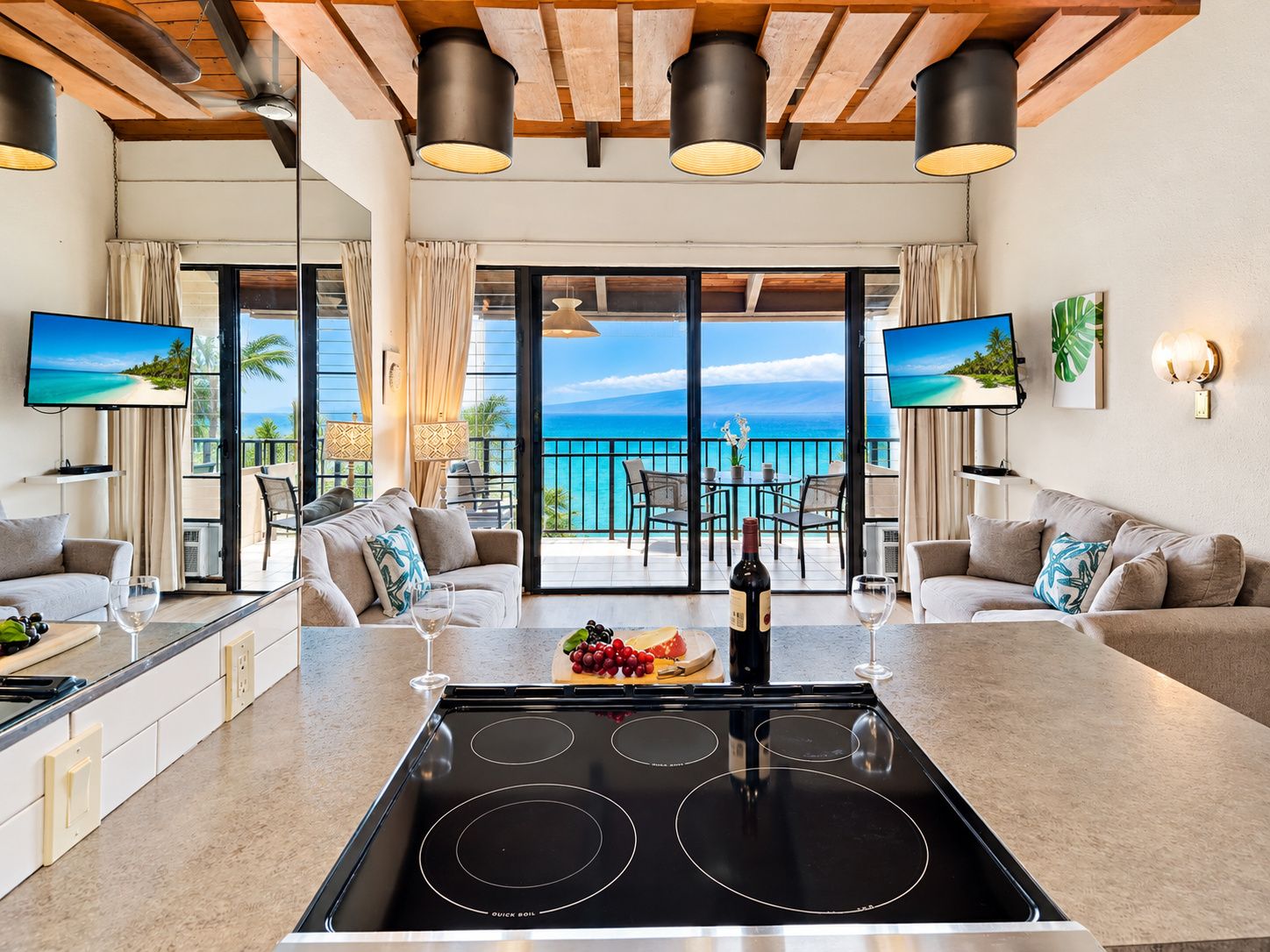 Una cocina moderna con una isla central, un comedor con vistas al océano y una sala de estar con sofá y televisor.