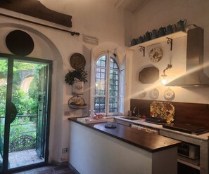 Une cuisine dotée d’un îlot central, d’une fenêtre donnant sur un espace verdoyant, ainsi que de divers éléments décoratifs, notamment des assiettes et une horloge murale.