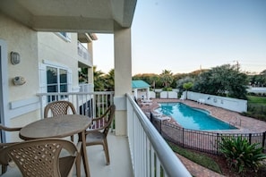 A residential balcony with a pool, outdoor furniture, and a view of a residential area.