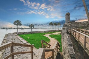 A coastal walkway with a stone wall, wooden stairs, and a grassy area leading to a body of water. - Ocean Reef 203 (St. Augustine)