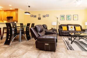 Een woonkamer met een leren bank, een eethoek met stoelen, en een keuken op de achtergrond.