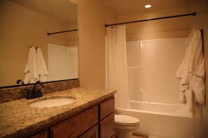 A bathroom with a granite countertop sink, wooden cabinets, a white toilet, and a bathtub with a shower curtain. - New upscale Southern Utah Getaway: 4 bed, 2.5 bath, sleeps 10 (Washington)