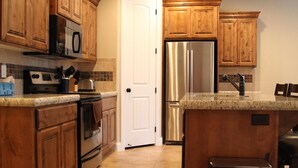 Una cocina con armarios de madera, electrodomésticos de acero inoxidable, encimera de granito y suelo de baldosas.
