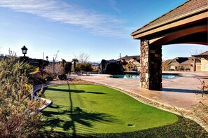 Enjoy a serene outdoor space with a putting green, swimming pool, and patio area surrounded by a beautifully landscaped garden.