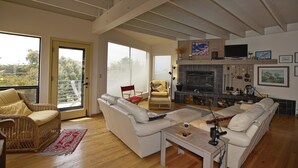 Un amplio salón con chimenea, asientos cómodos y grandes ventanales que ofrecen vistas al exterior.
