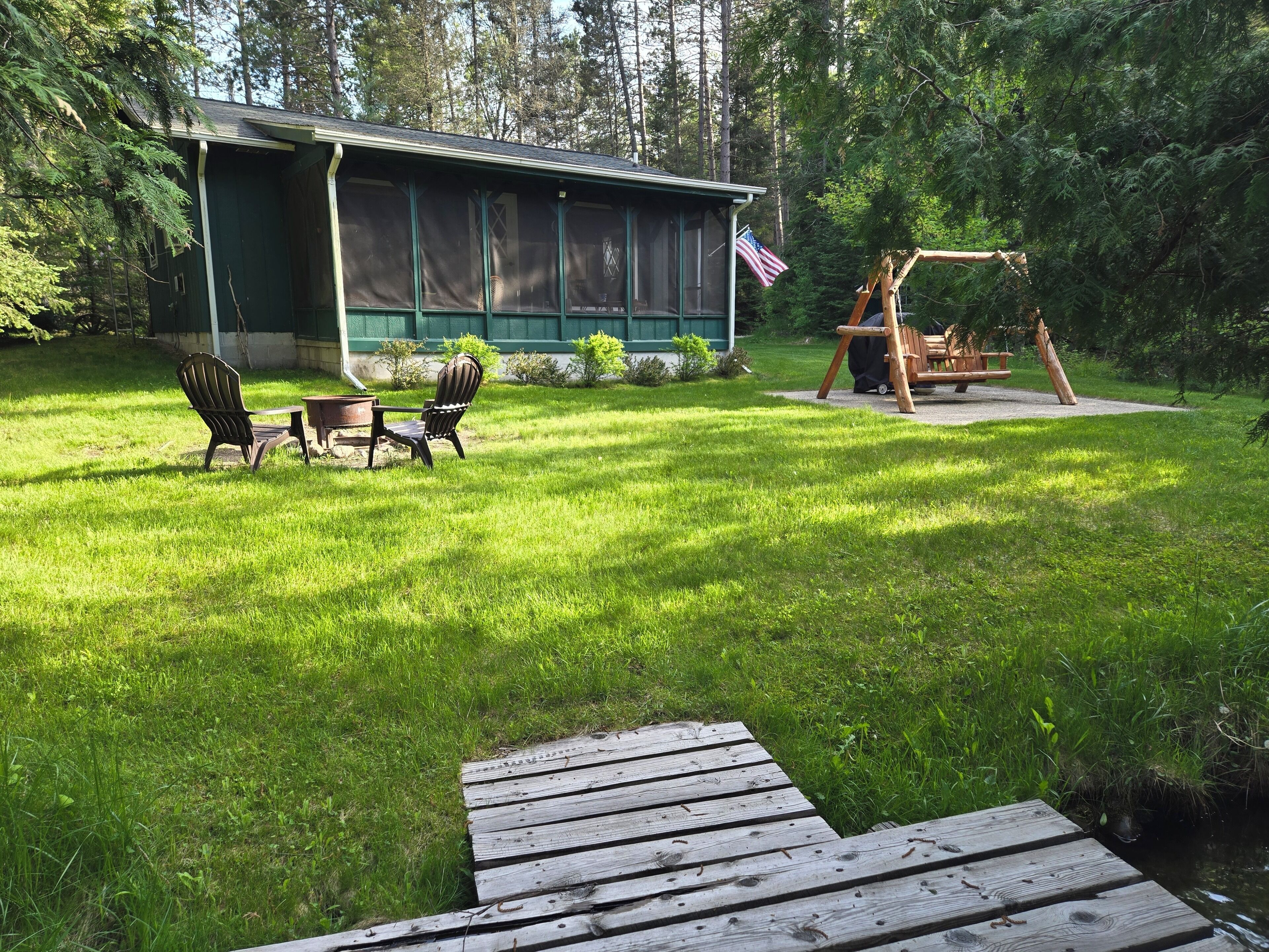 Een chalet met een overdekte veranda, buitenmeubels en een schommel.