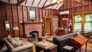 A cozy cabin interior with a fireplace, wooden walls, a bookshelf, and a dining area.