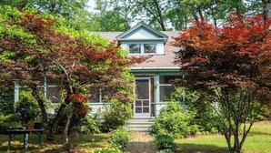 A house with a front porch, surrounded by lush greenery and trees with autumn leaves.