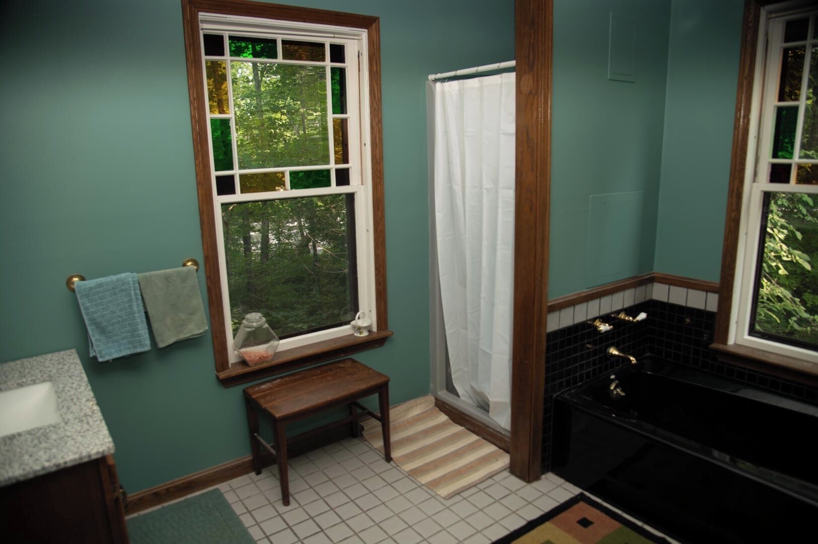 Une salle de bain avec une fenêtre, une baignoire et un petit banc en bois.