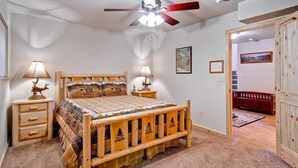 A bedroom with a wooden bed, two bedside tables with lamps, a ceiling fan, and a door leading to another room. - Explorers Retreat (Yosemite National Park)