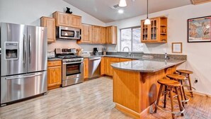 A modern kitchen with stainless steel appliances, wooden cabinets, and a central island with stools. - Explorers Retreat (Yosemite National Park)