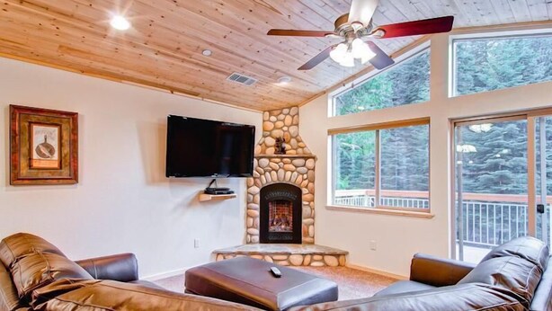 A living room with a stone fireplace, leather sofa, and large windows. - Explorers Retreat (Yosemite National Park)
