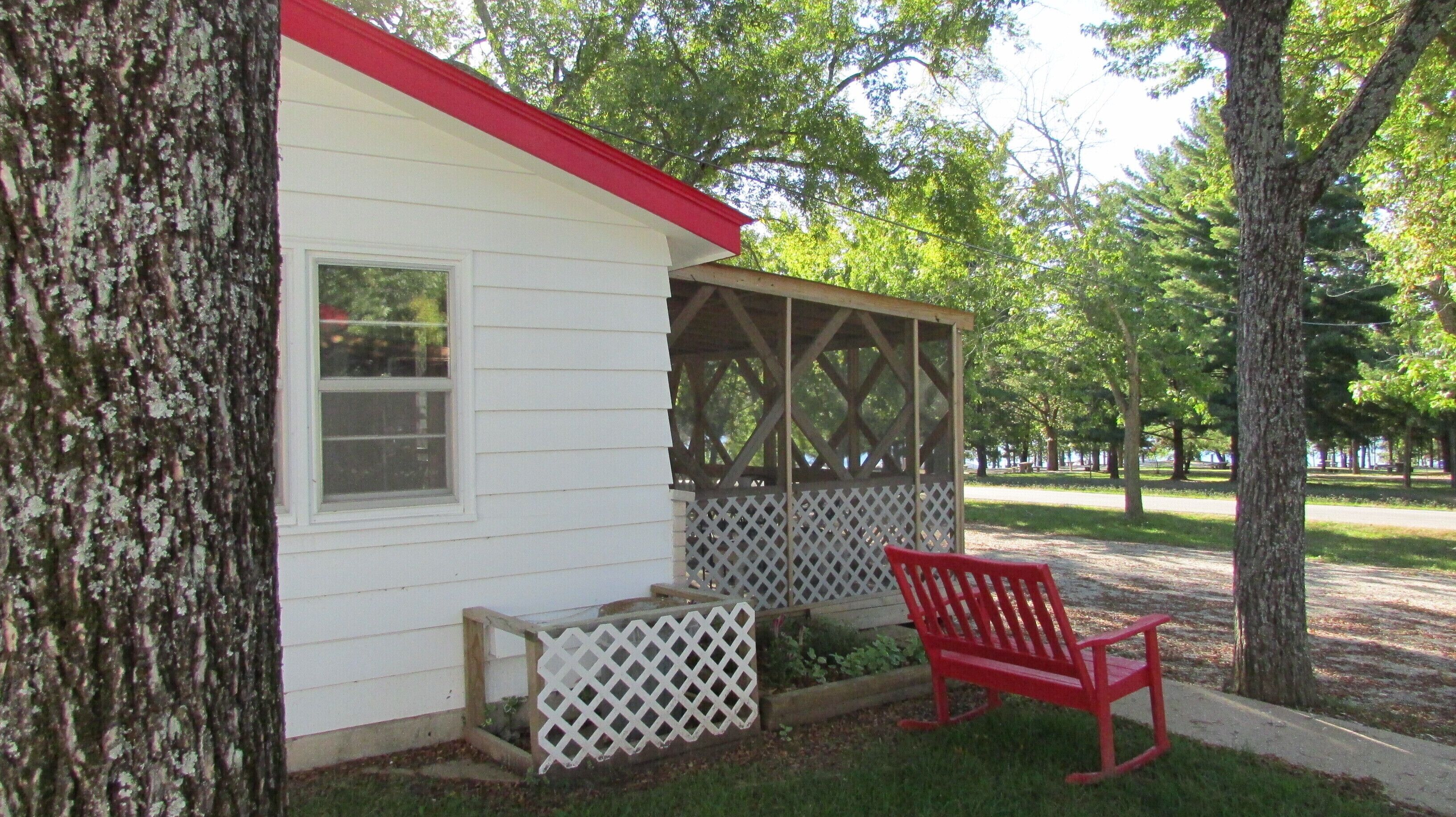 A small white building with a red roof, a wooden bench, and a lattice-covered structure.