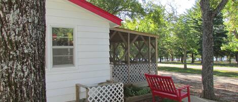 A small white building with a red roof, a wooden bench, and a lattice-covered structure.