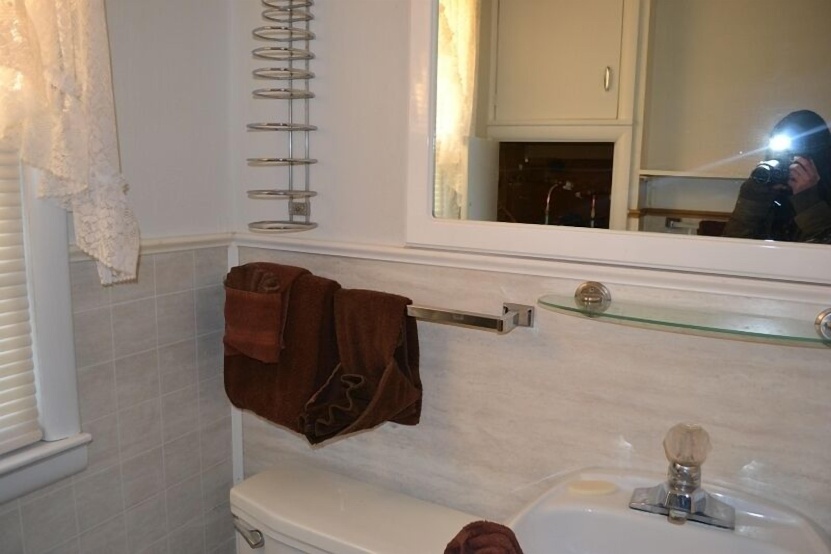 A bathroom with a white toilet, a glass shelf above the sink, and a towel rack with a brown towel.
